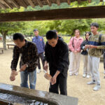 神社の手水舎で手順に沿って手を清める実習生の様子