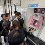 JR伊部駅の券売機前で切符の購入方法や時刻表の見方を学ぶ実習生