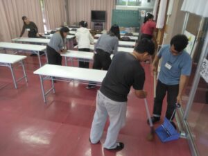 雑巾を使って机の上を拭いている生徒らと、ほうきを持って床を掃いている技能実習生らの姿。