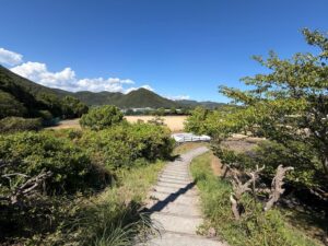青空の下、山や木々に囲まれた階段とグラウンドが見える風景